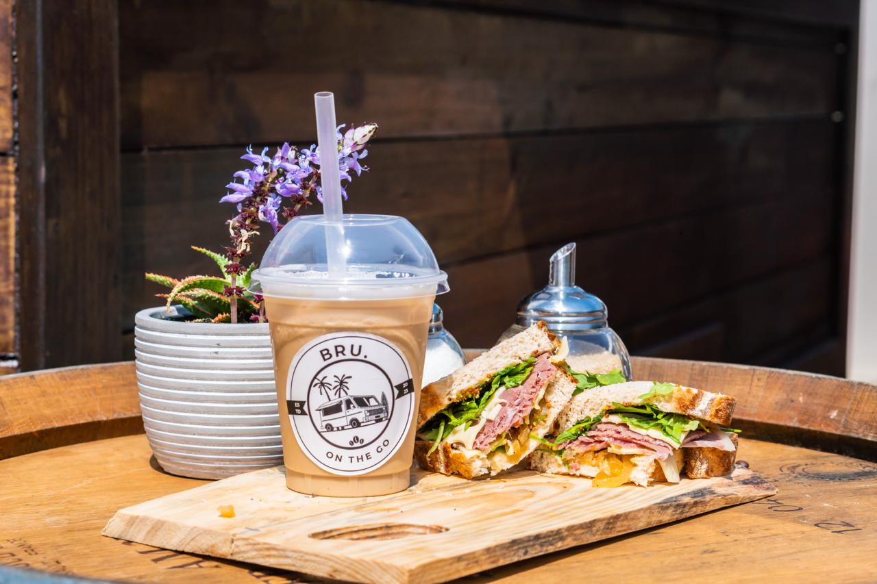 BRU. iced coffee paired with a fresh sandwich on a wooden board